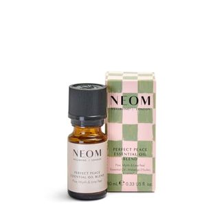 A small glass bottle of essential oil in front of a pink and green checkered cardboard box