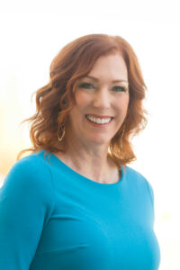 A headshot of a woman with curly red hair smiling at the camera