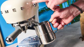 a cream-colored retro espresso machine by italian brand smeg is photographed against a blue background with a bag of coffee beside it