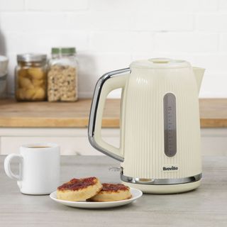 Cream Breville kettle next to cup of tea and crumpets with jam