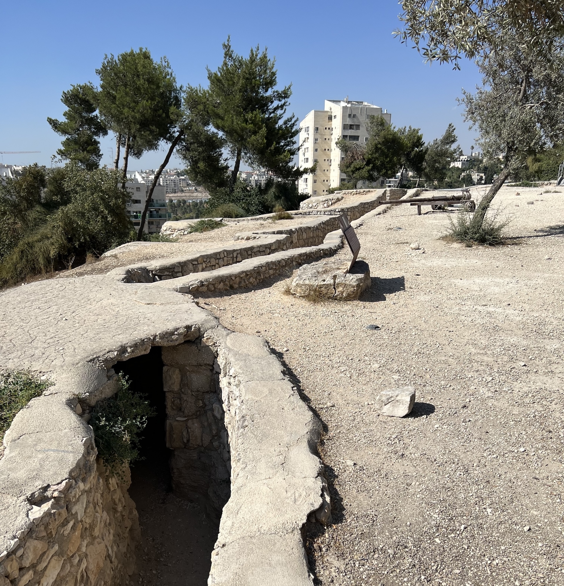 We see a stone trench by a dirt surface with a modern city in the background.