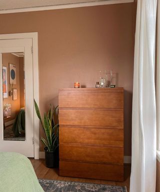 A brown wooden drawer set next to a mirror and curtains