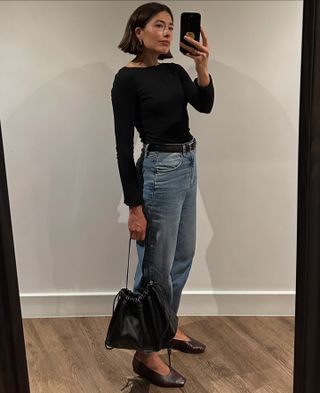 British style influencer Lucy Alston poses for a mirror selfie wearing a black boatneck top, black belt, jeans, and black square-toe flats.