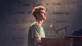 Et billede fra filmen tick, tick...BOOM! Andrew Garfield sidder ved et klaver med en mikrofon foran en baggrund med tekst og musiknoder.