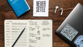 Photo illustration: Desk with earbuds, agenda, "Never settle" notebook