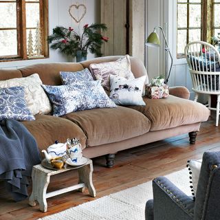 A neutral living room with a brown velvet sofa and patterned cushions and wooden table and chairs