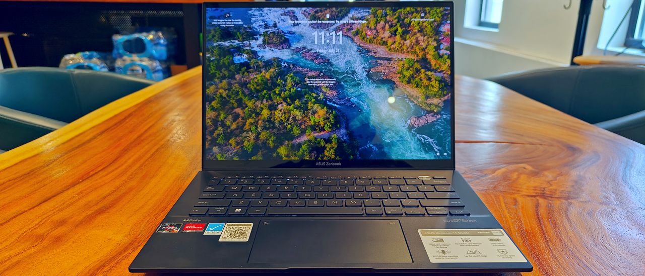 Asus Zenbook 14 OLED UM3402Y open on a wooden desk showing the lockscreen on the display.