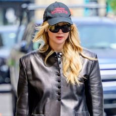 Jennifer Lawrence wearing a black "Twilight: Breaking Dawn" baseball cap, black Kallmeyer leather blazer, white pants, and a red bag in NYC.
