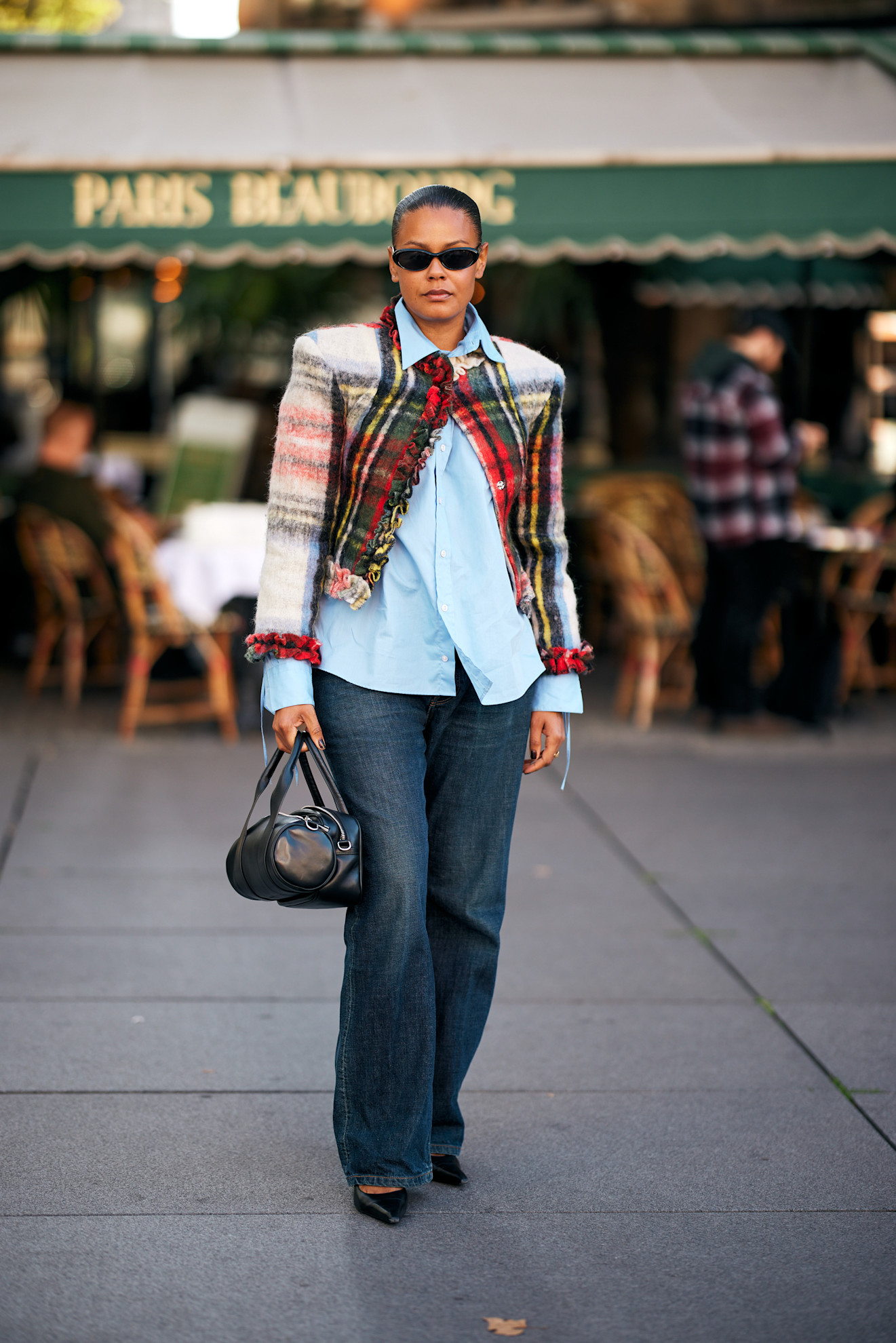 PARIS, FRANCE - JULY 08: A guest wears a short-sleeve white knit top layered with a blue and white boucle tweed vest featuring pearl trim and gold buttons, dark blue straight-leg jeans, black leather ballet flats, oversized black sunglasses, and a long pendant necklace with gold medallions outside the Chanel show during the Haute Couture Fall/Winter 2025/2026 as part of Paris Fashion Week on July 08, 2025 in Paris, France. (Photo by Valentina Frugiuele/Getty Images)