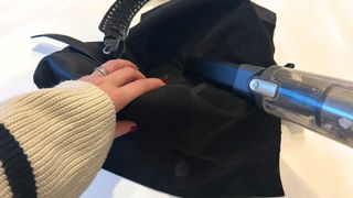 The inside of a leather bag being held open by a hand and vacuumed with a hand-held vacuum