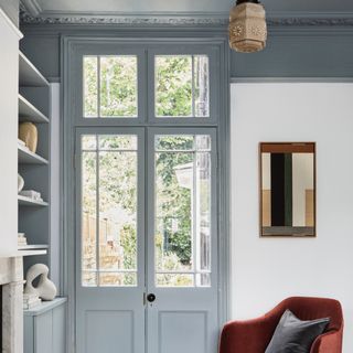 living room ceiling ideas, living room with blue/grey woodwork, walls and ceiling, vintage pendant, rust armchair, mirror, shelving, view outside via French doors