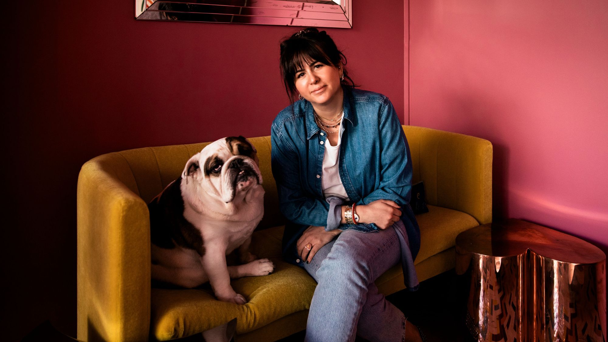 jewellery designer roxanne first and her dog sitting on a yellow sofa