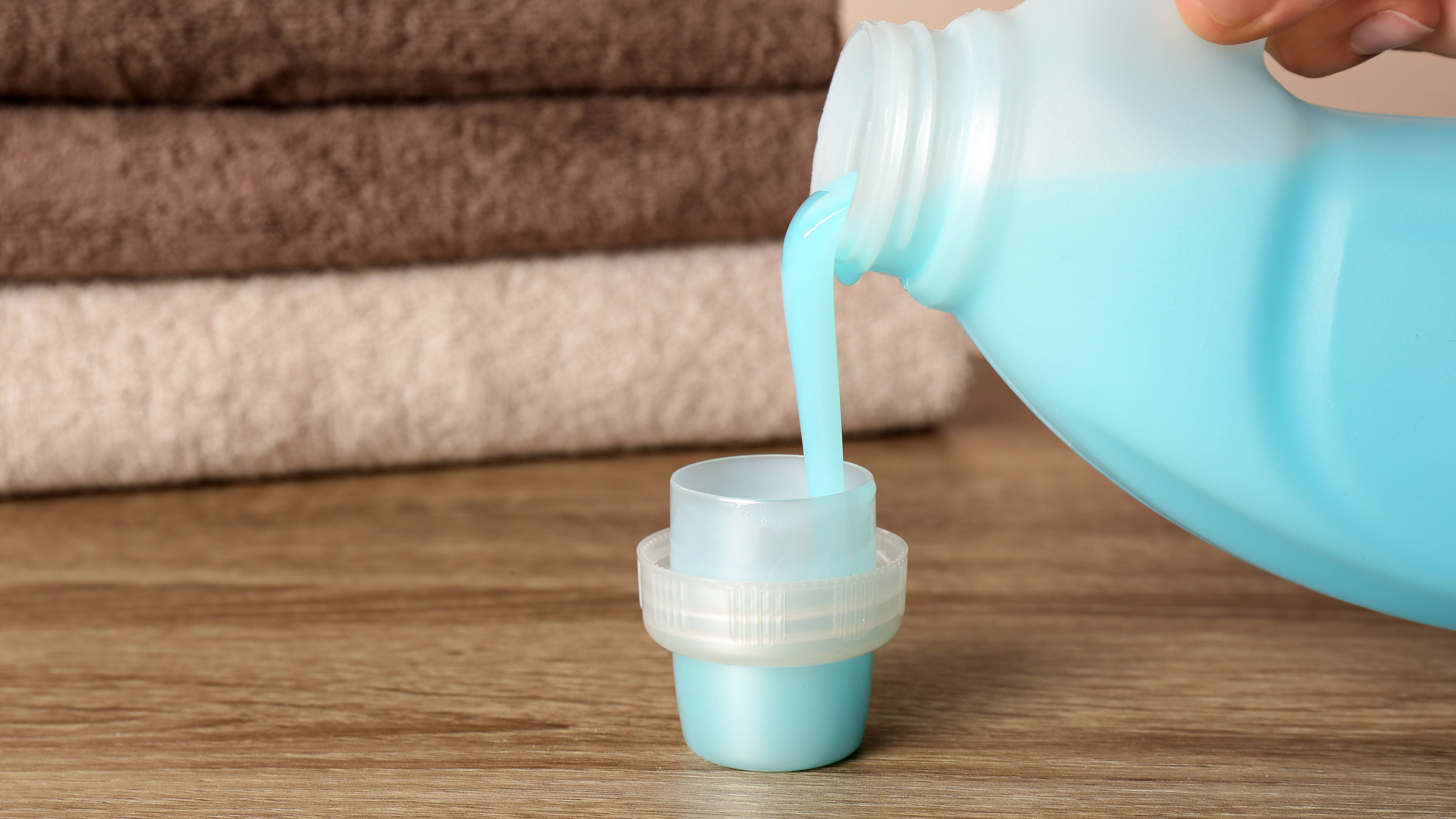 Fabric softener being poured into the cap in front of towels