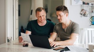 male couple looking at laptop screen sat at kitchen table