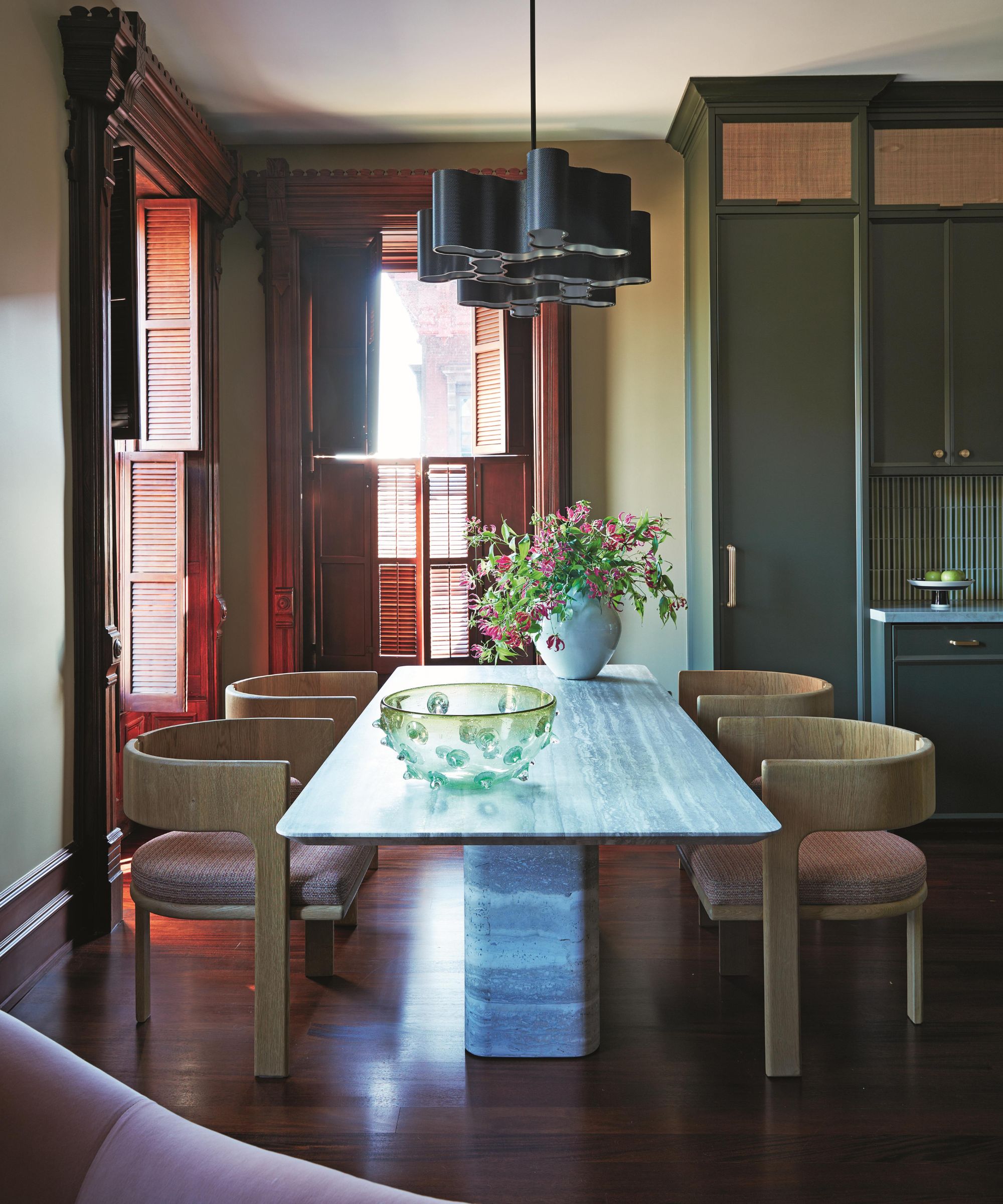 a colorful dining room in a new york apartment with marble table, curved chairs, and original mahogany windows