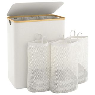 A beige laundry basket with lid and three removable mesh bags filled with laundry beside it