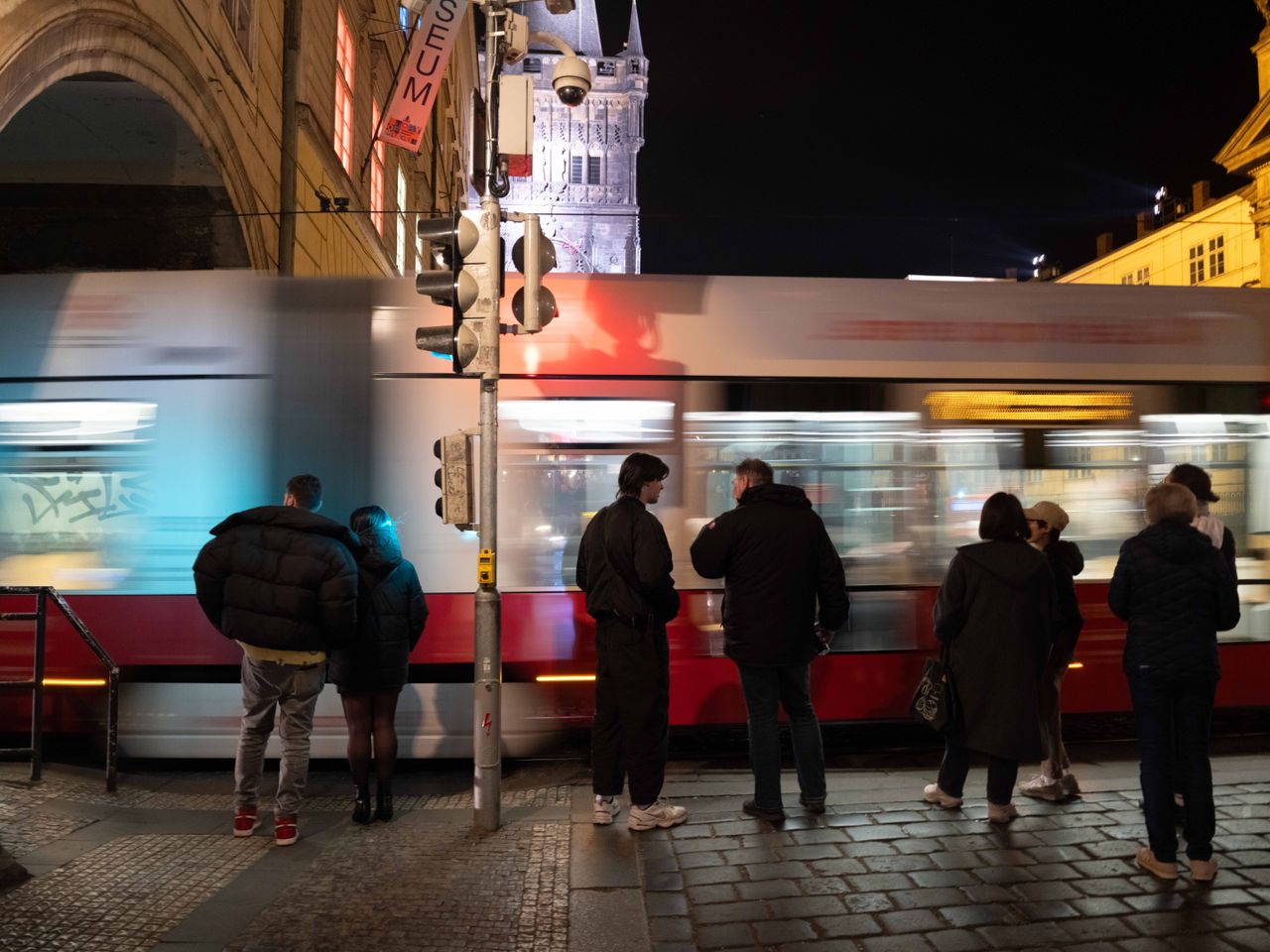 A tram whizzes past people as they wait to cross the street