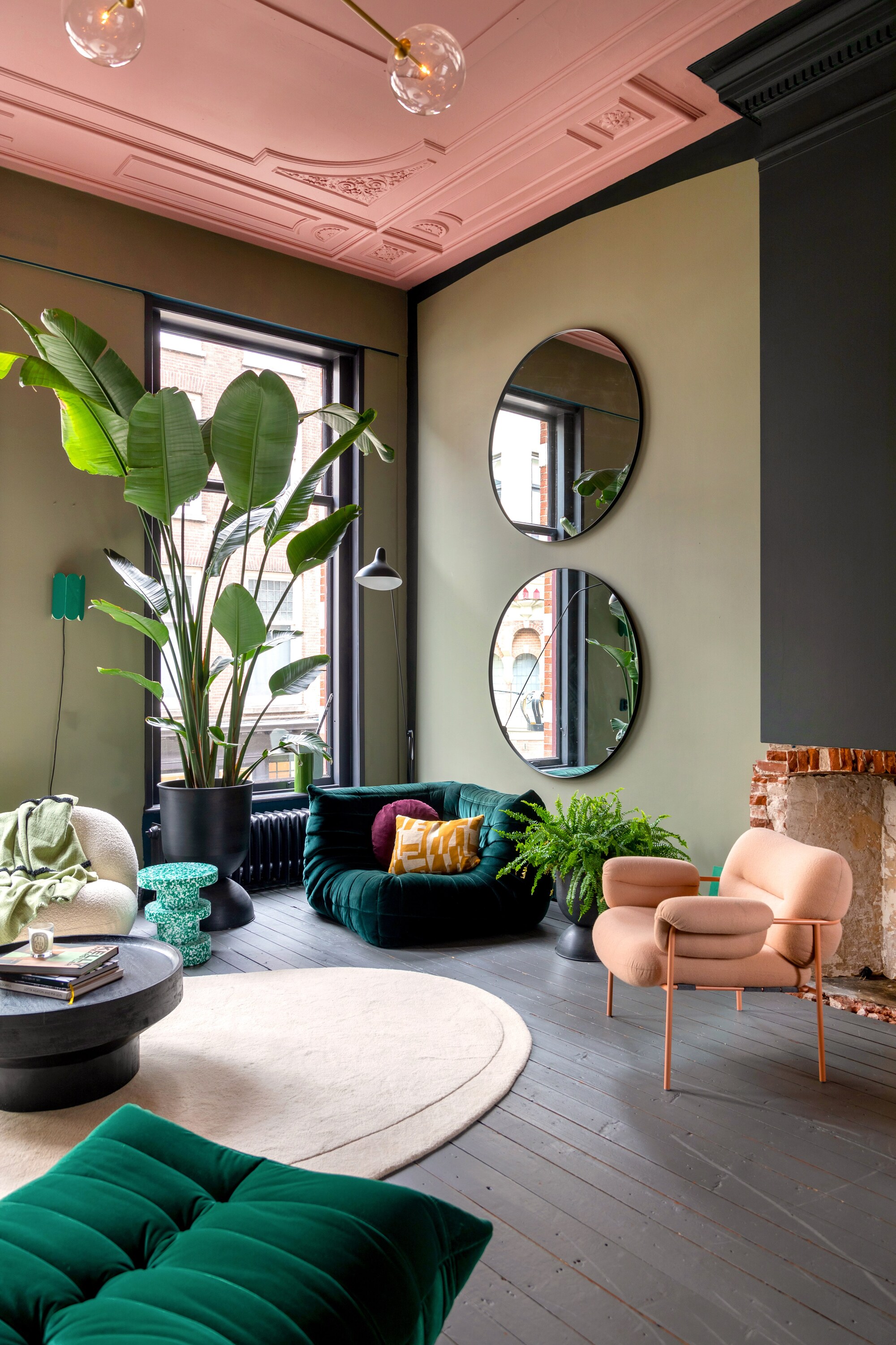 High ceiling living room with sage green walls, black architraves and cornicing, and a soft pink painted ceiling. The space is furnished with modern pieces.