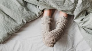 Two feet poking out under a duvet at the end of the bed wearing cosy bed socks