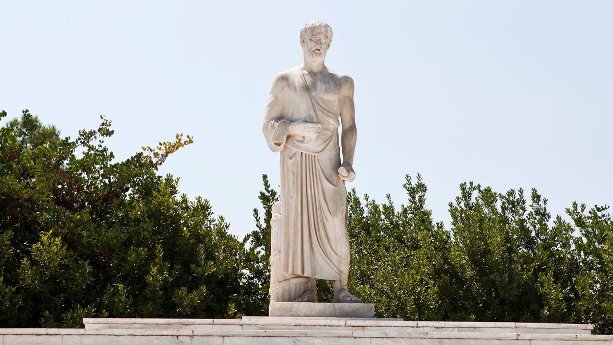 A white marble statue of Hippocrates standing at the top of a set of marble stairs near some trees and bushes