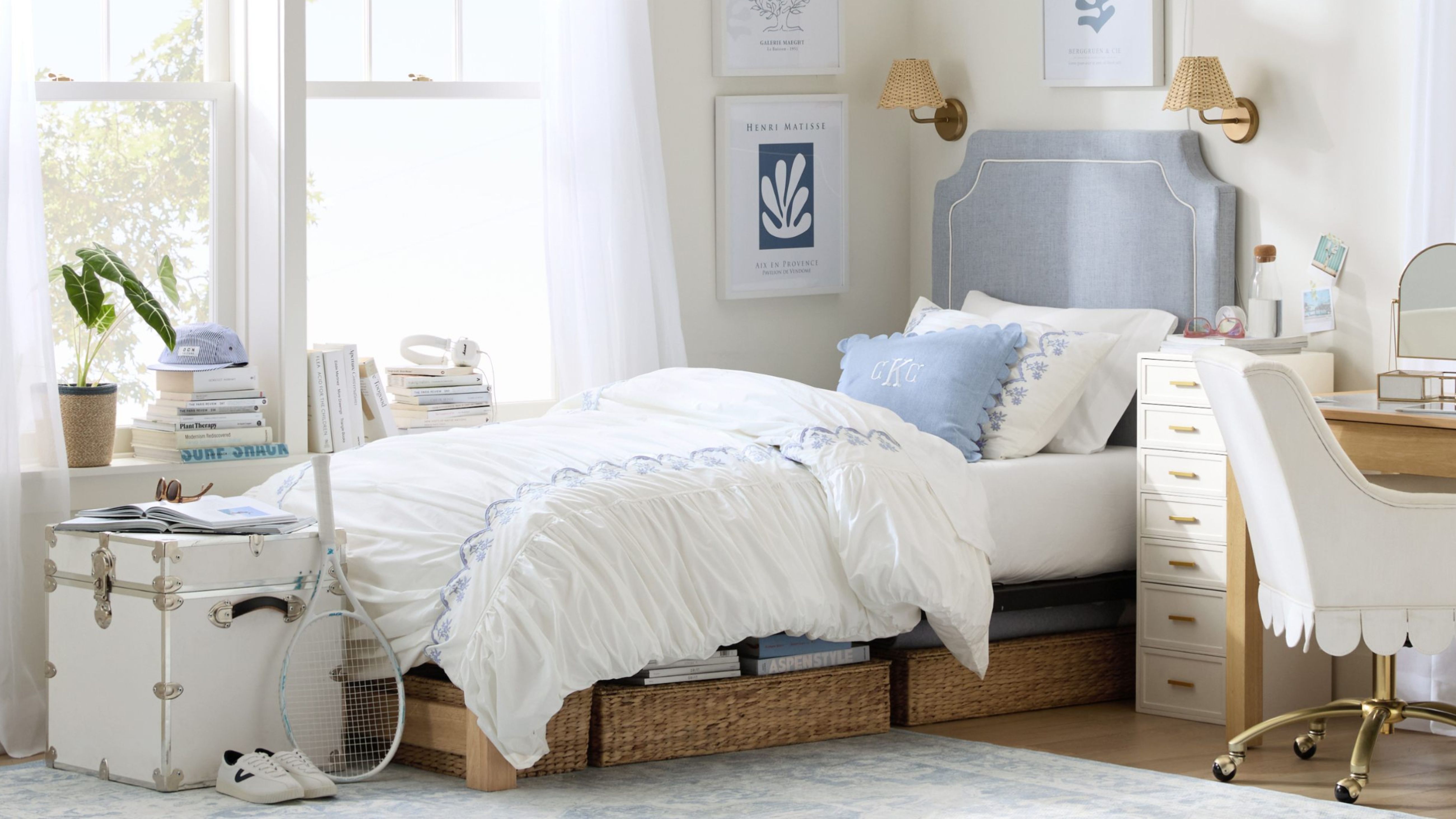 Relaxing dorm room with a cream and periwinkle color scheme and natural woven accents, seen in under bed storage and lamp sconces.