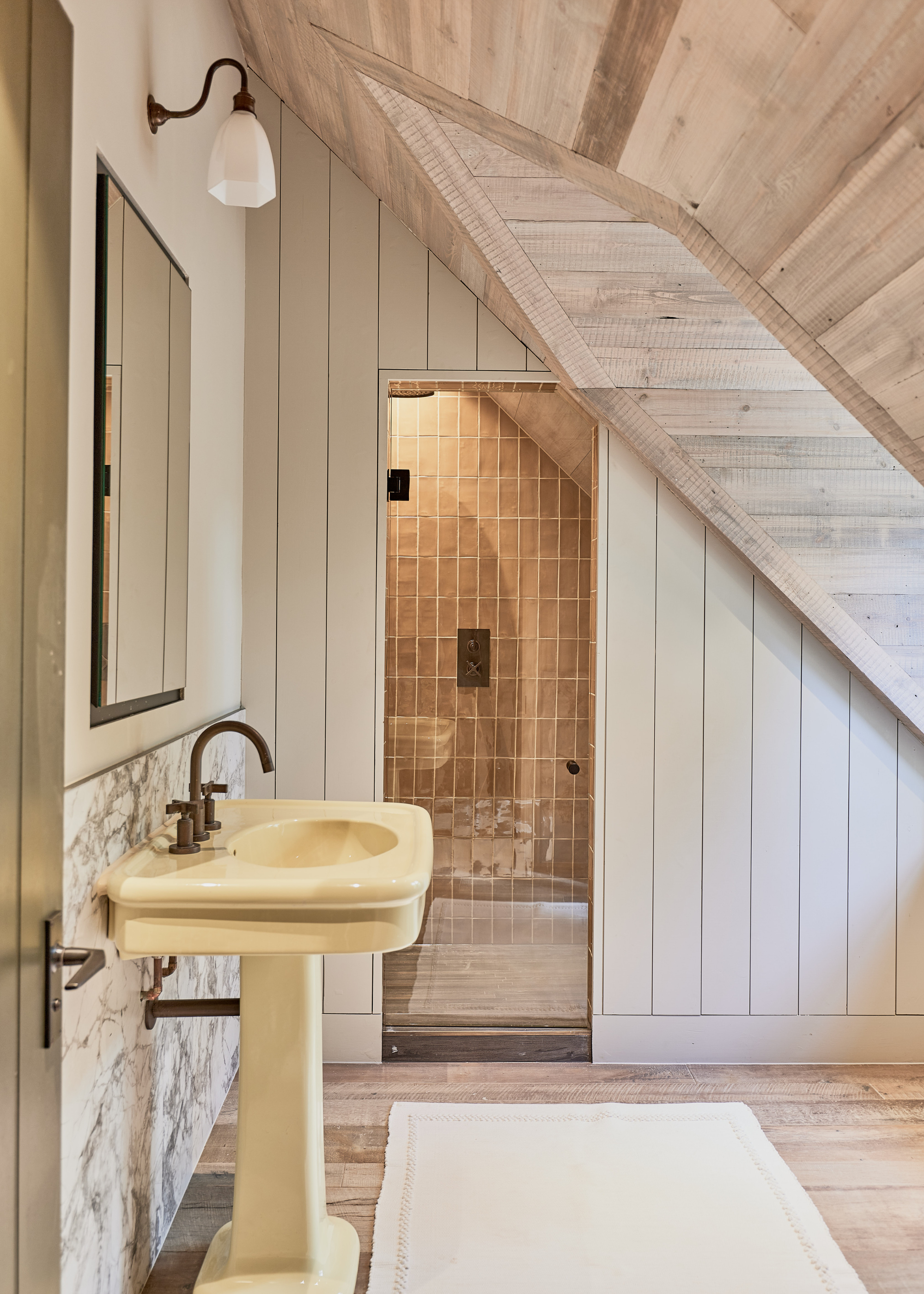 gorgeous bathroom in an attic with a small shower, yellow pedestal sink and reclaimed wood floorign