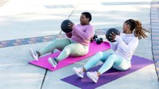 Two women performing sit-ups with medicine balls as part of an abs workout