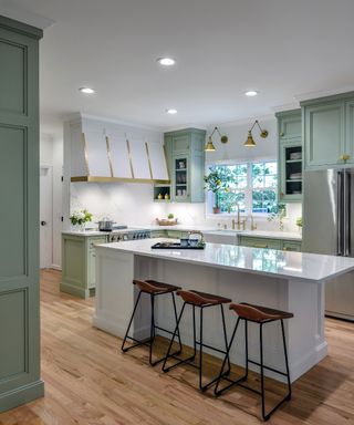 Bakes & Kropp pale green and white kitchen with brass accents, white kitchen island, hardwood floor, bar stools,