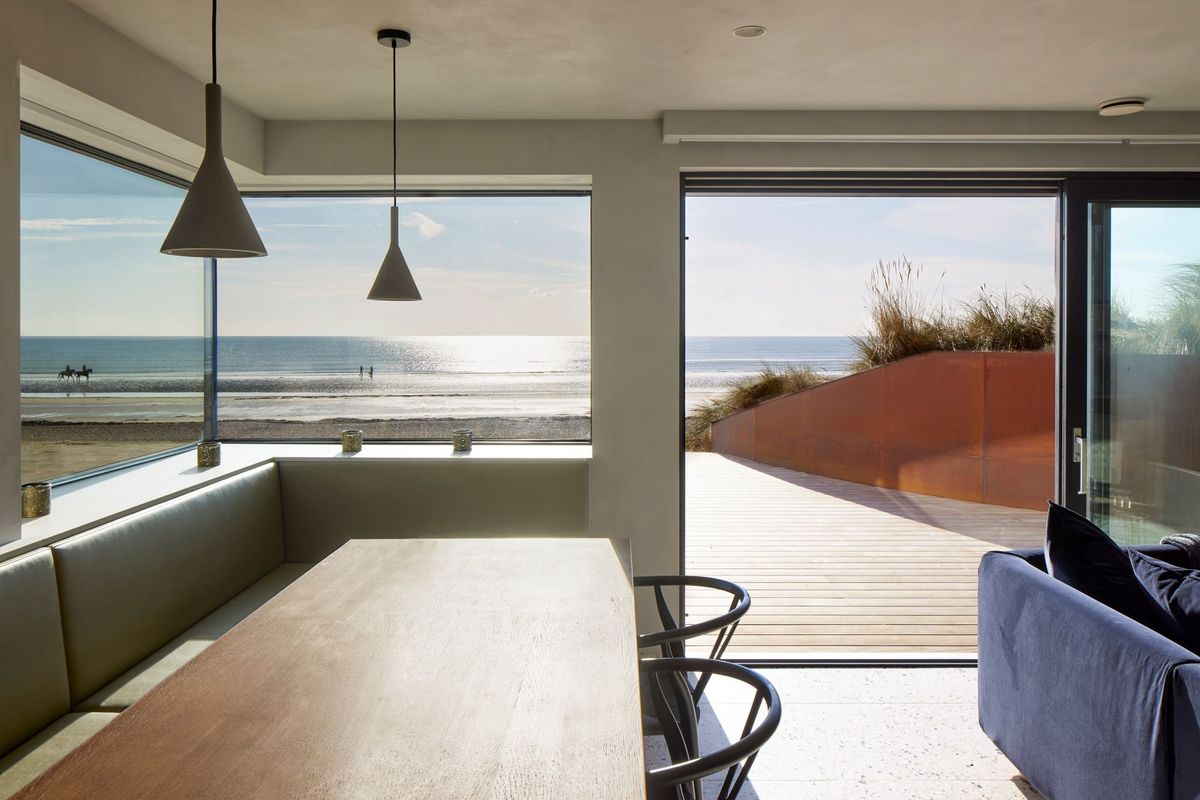 A view of the coast from the open plan living area with a dingin table and chairs in the foreground and bifolding doors open to the beach outside