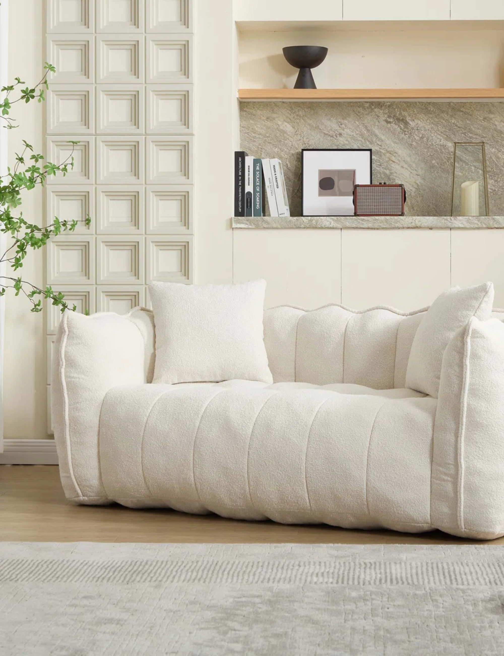 Small cream channel tufted 'boneless' couch styled inside of wood-floor living room area with a grey area rug and assorted decorative objects