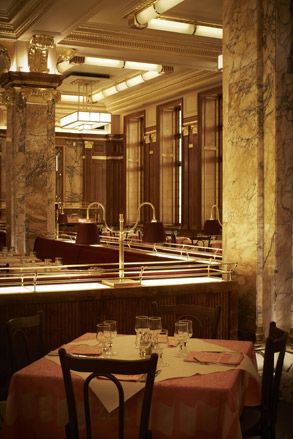 A restaurant with decorated tables, wooden chairs, marble pillars, wall mirrors and a square chandelier.