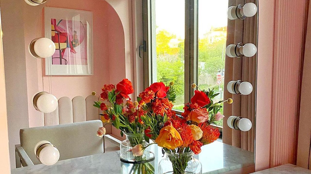 Makeup mirror with exposed bulbs, and fresh flower bouquet in orange and rouge hues on counter