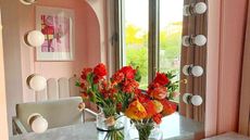 Makeup mirror with exposed bulbs, and fresh flower bouquet in orange and rouge hues on counter
