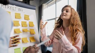 woman stood by whiteboard and post-its discussing marketing