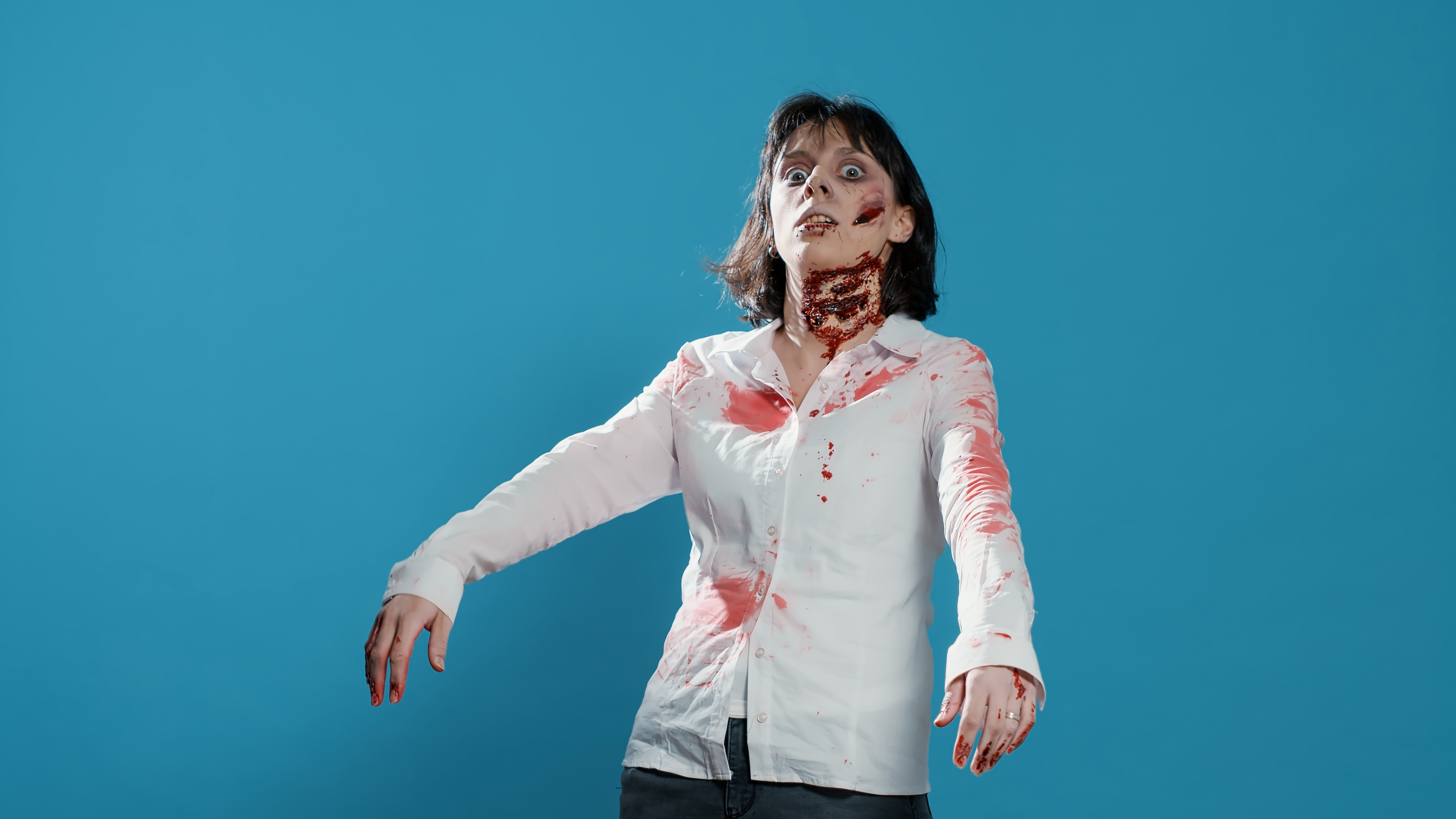 A woman dressed and posing as a zombie with blood stains on her shirt and a wound in her neck
