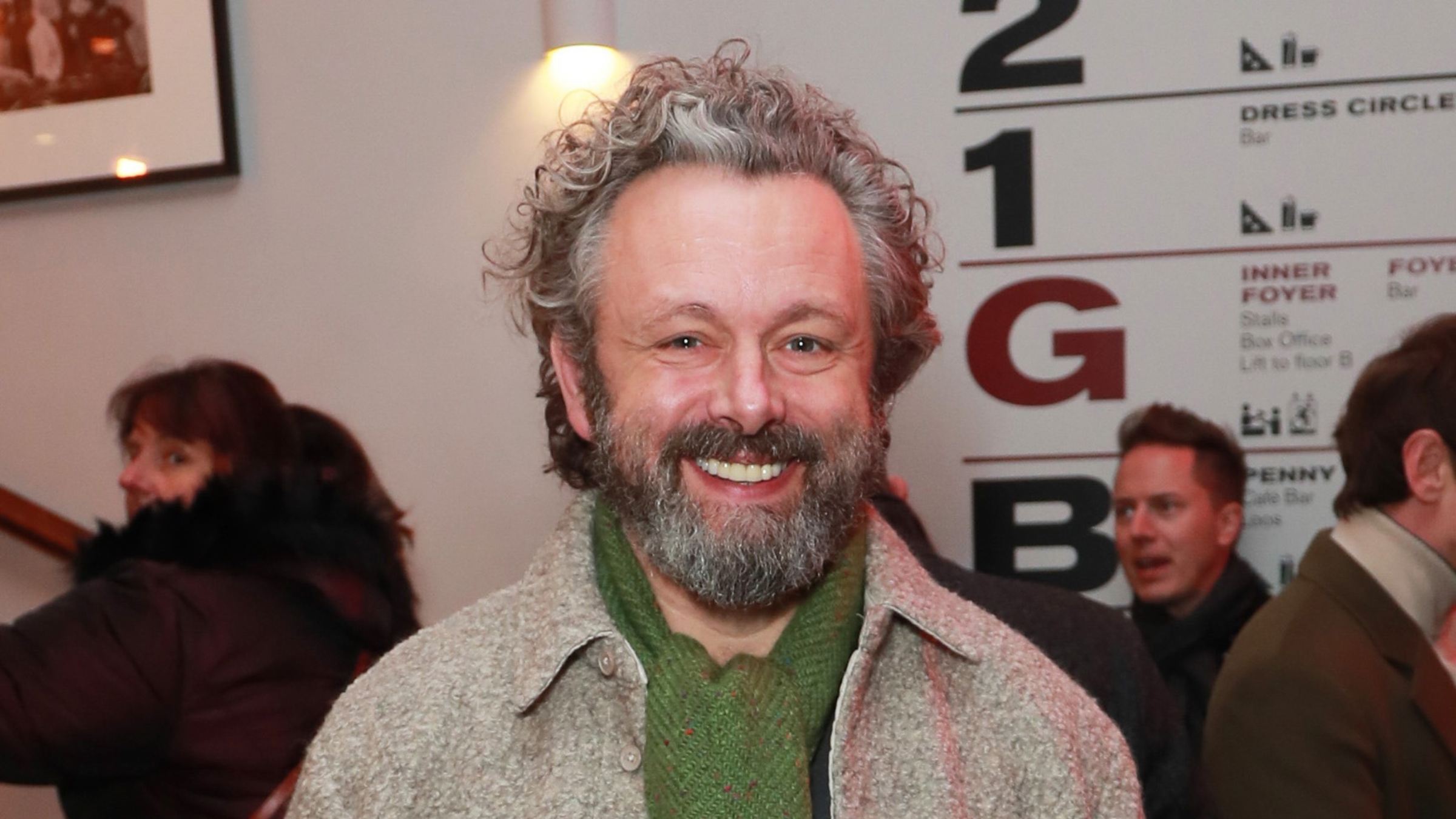 Michael Sheen wearing green scraf and grey coat.