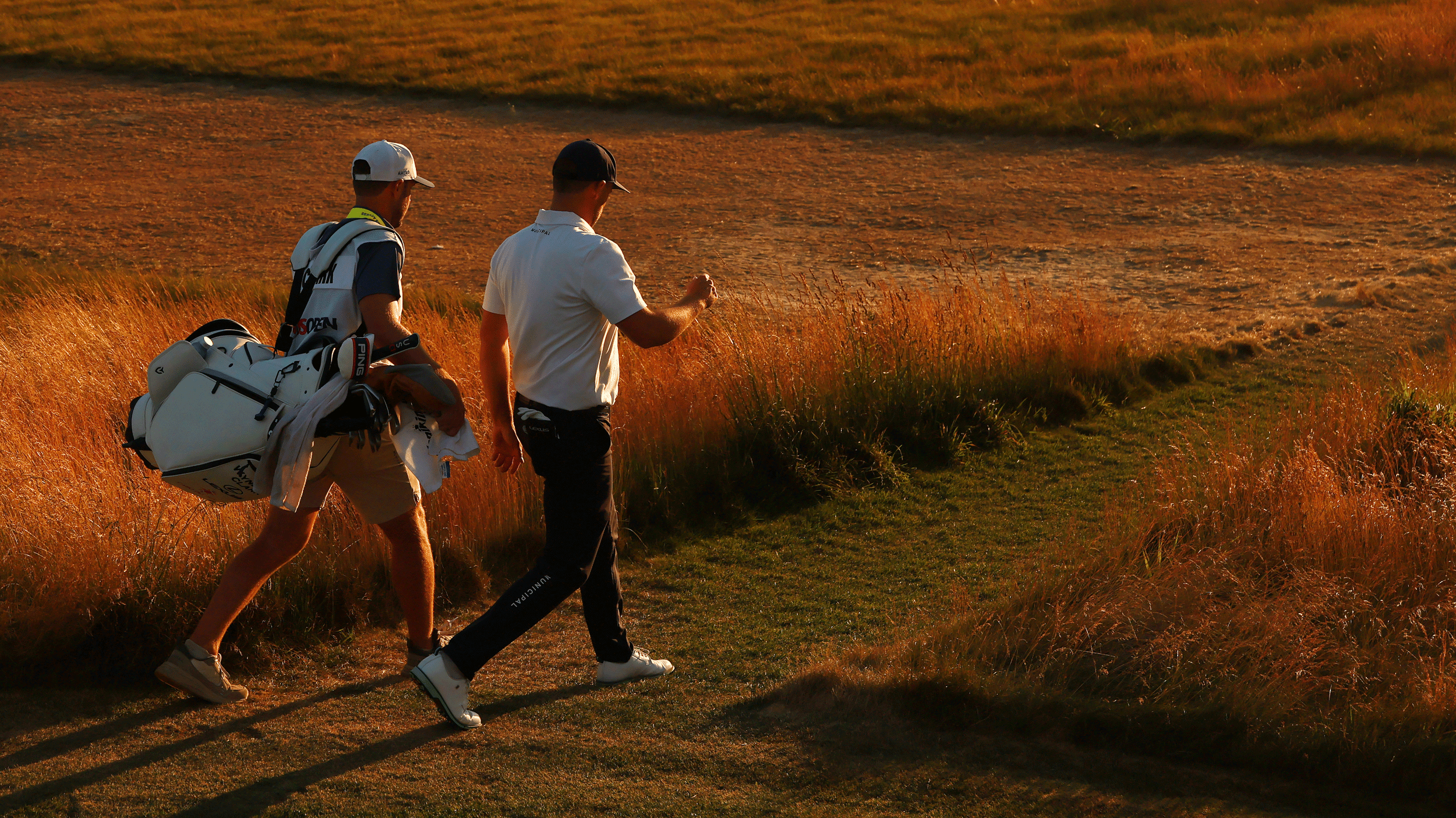 Wyndham Clark (right) and his caddie Dave Pelekoudas walk along during sunset in round three of the 2026 US Open