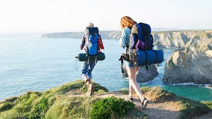Two people wearing backpacks by the coast