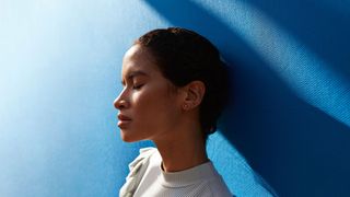 A woman leans against a blue wall and performs the 5-4-3-2-1 method