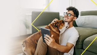 Man sitting on floor looking at phone whilst being licked by a dog