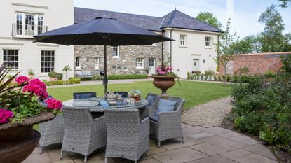 Charming outdoor garden and patio area featuring a dining set and antique-style wall lights flanking the exterior.