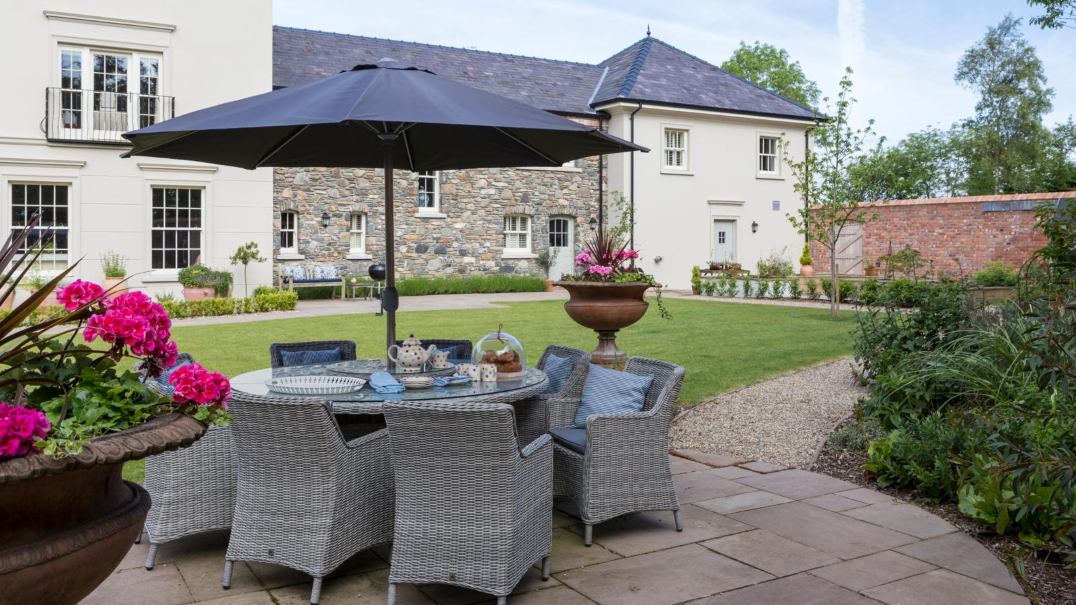 Charming outdoor garden and patio area featuring a dining set and antique-style wall lights flanking the exterior.
