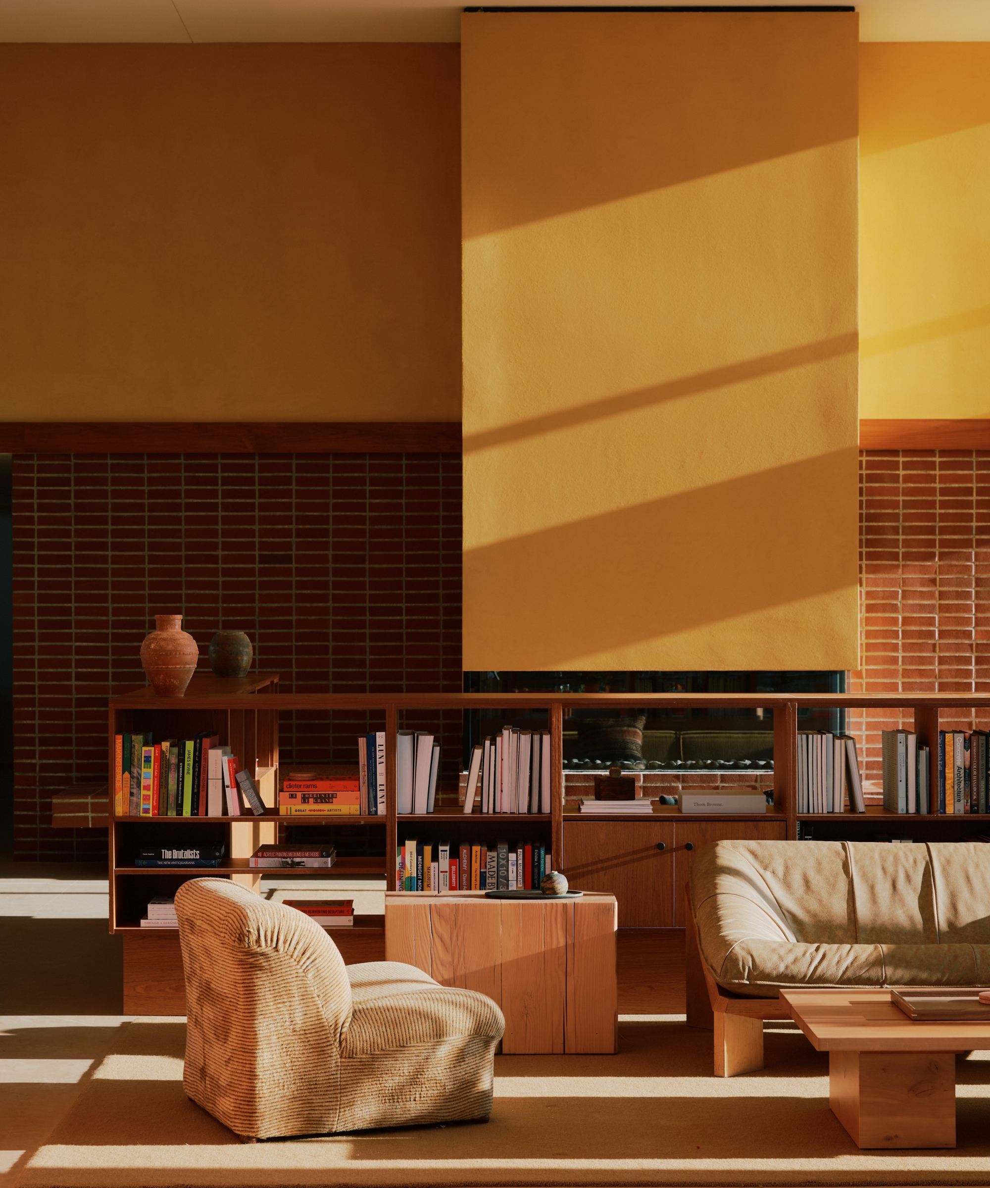Living room with harvest gold walls, walnut shelving, terracotta tile fireplace, low wood furniture, and warm afternoon sunlight.