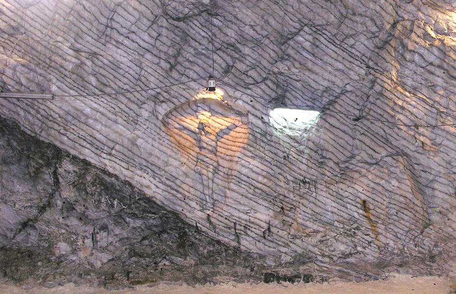 An image of a crucifix is carved into a stone face with a light illuminating the figure of Jesus on the cross.