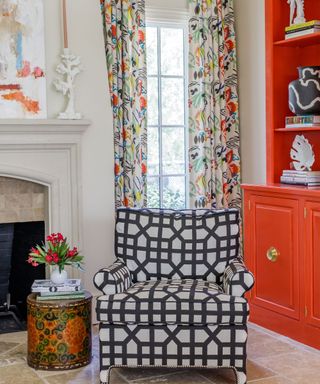 Colorful corner in living room with orange cabinetry and patterned chair and curtains