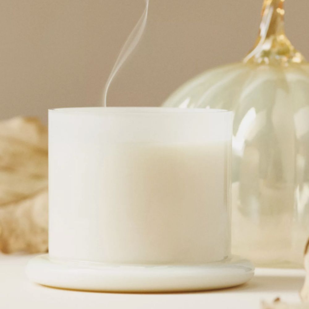 White candle with a glass pumpkin in the background
