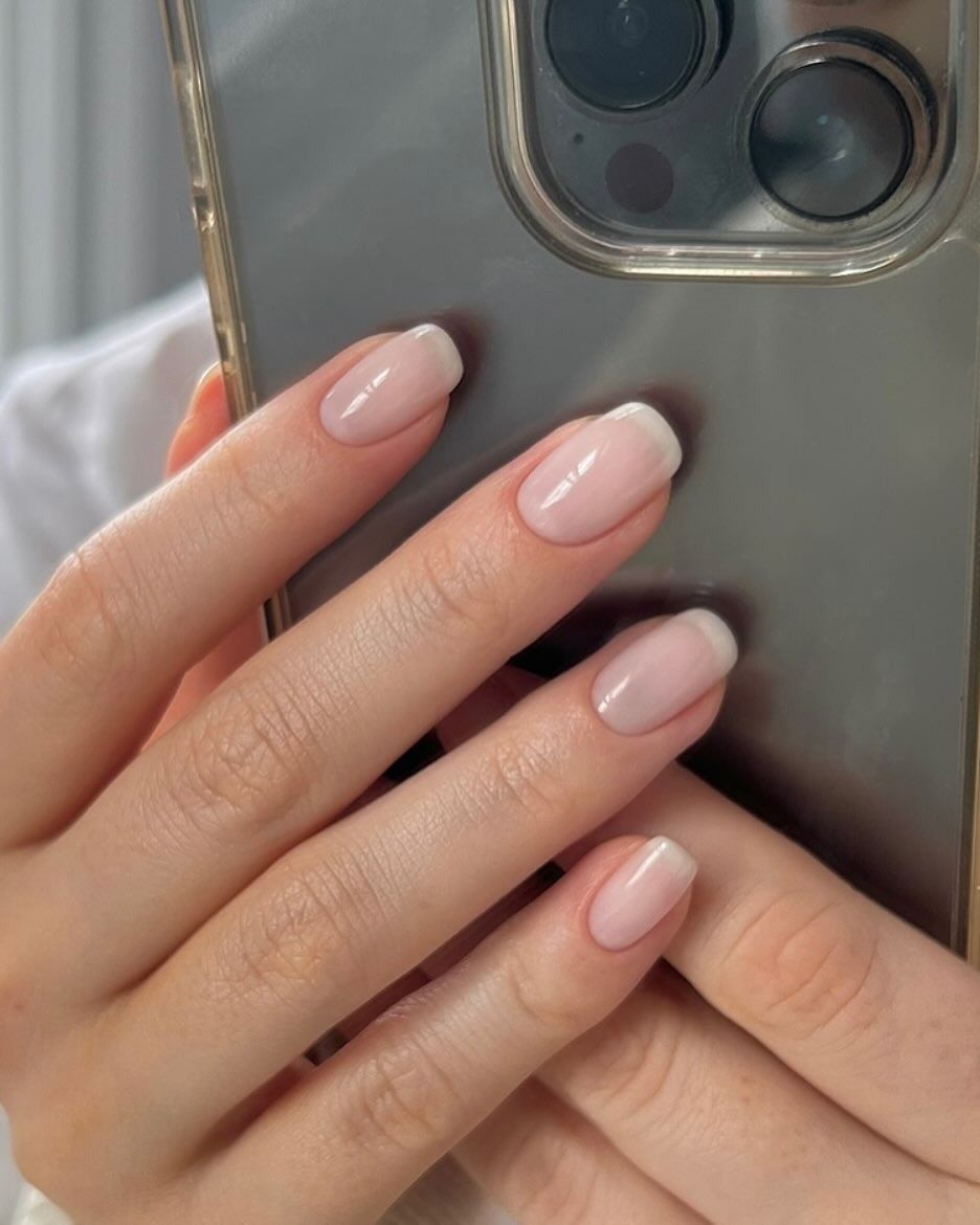 A woman taking a mirror selfie of her subtle French manicure