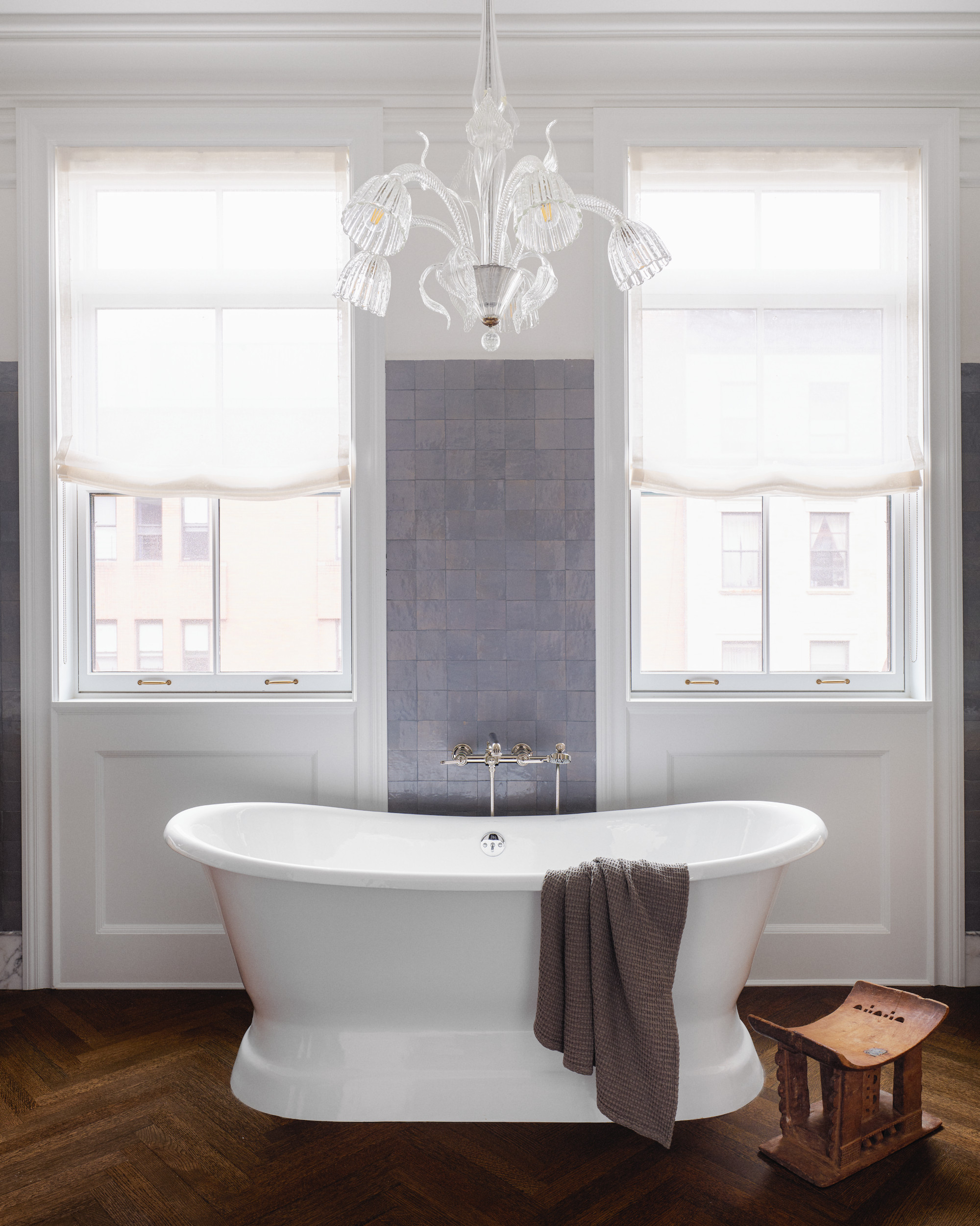 Bathroom with white panelling, lavender tiles, wood floor, white freestanding bathtub and glass chandelier