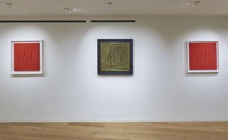 Three canvases on display. A grey canvas in the centre and red on either side.