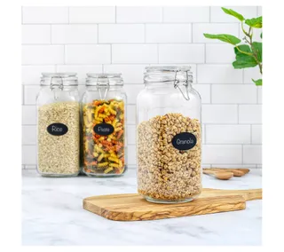 Three large glass storage jars with lids on a white kitchen counter against a white tile wall. Filled with dried food goods.